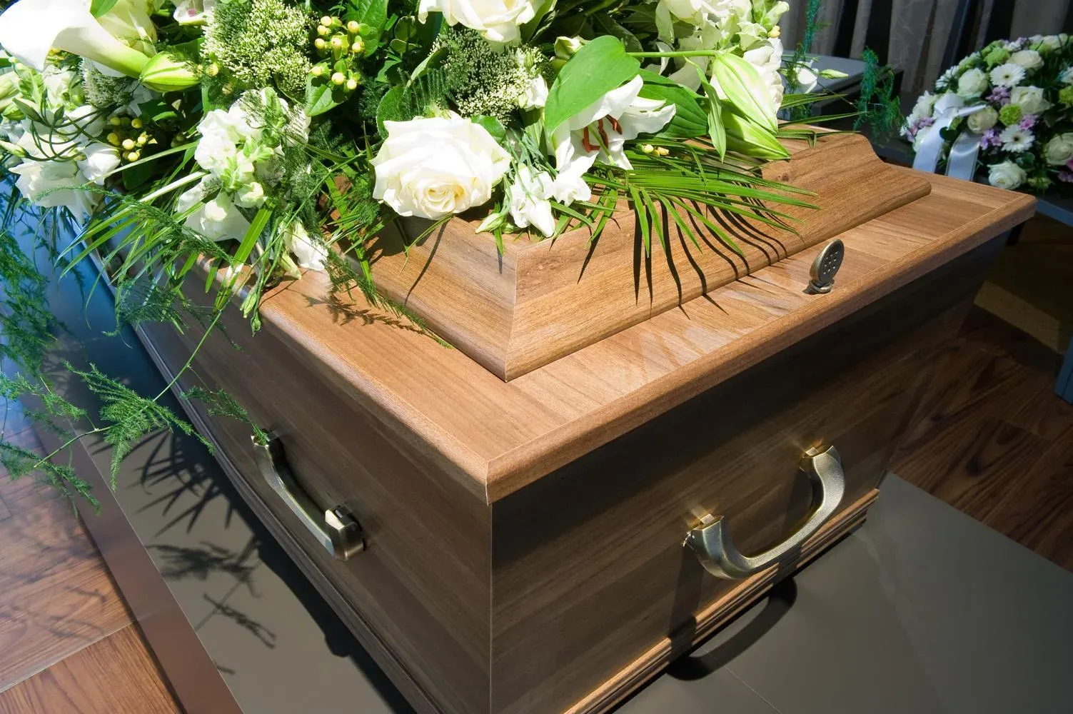 Gros plan sur un cercueil en bois surmonté d'un bouquet blanc